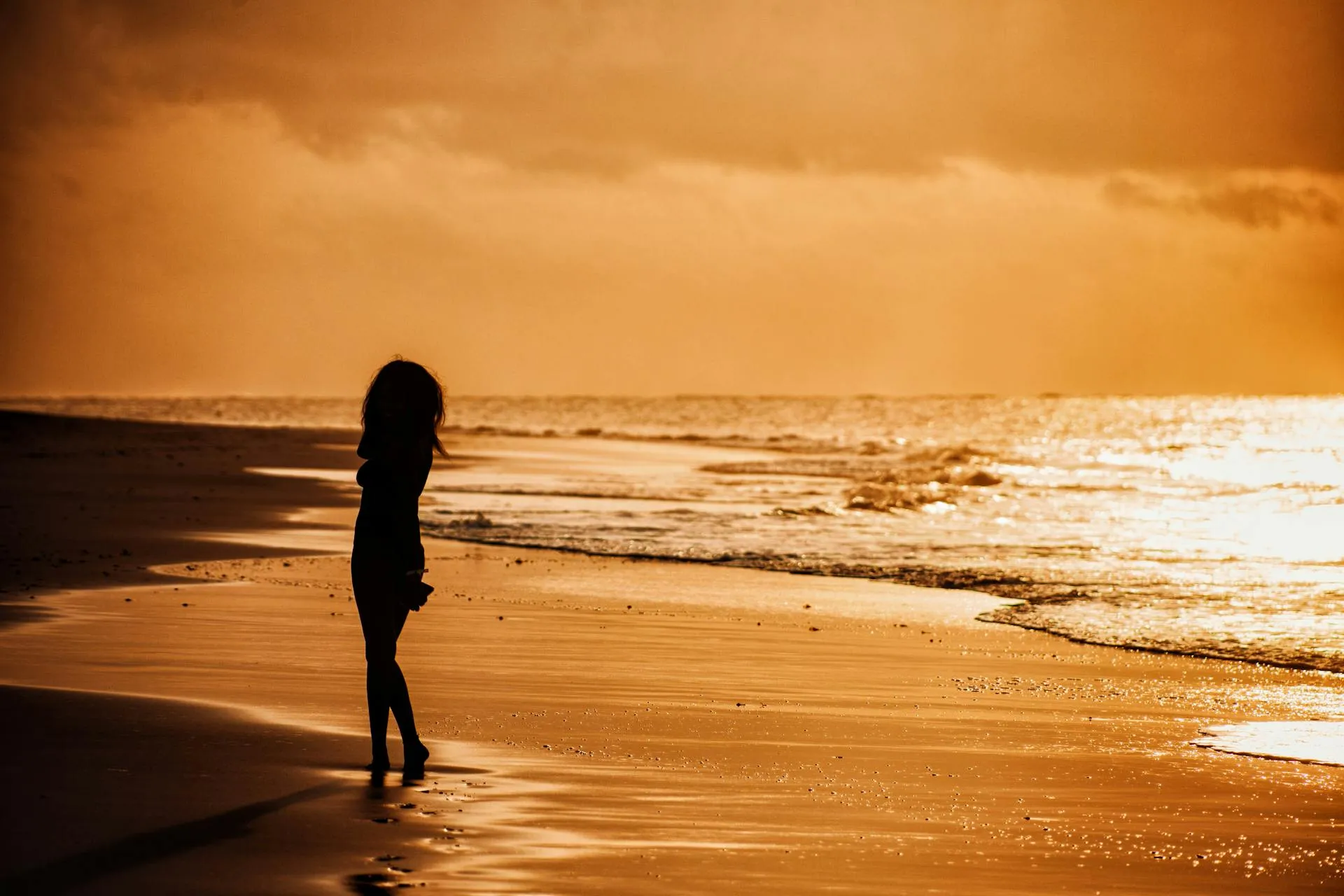 Woman walking along the beach at sunset